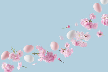 Pink and white Easter eggs adorned with cherry blossom branches, levitating against a blue background. Easter themed Springtime nature decoration concept. Copy space.