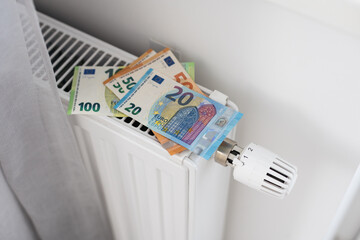 A heating radiator battery with a temperature controller from which 50 euro bills stick out. The...