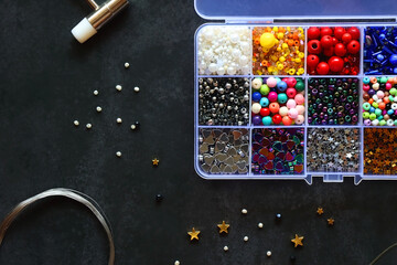 Box with colorful beads, string, wire, chain, scissors, pliers and hammer on dark background....