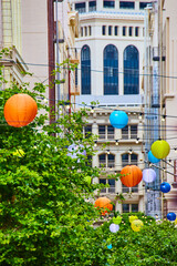 Green tree connected to string lights and colorful lanterns with city building background in San...