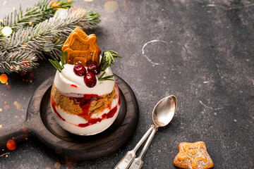 A glass of Christmas dessert with gingerbread cookies, whipped cream and cranberries on grey background, copyspace for text