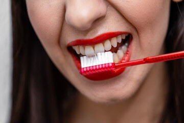 A woman brushing her teeth with a red toothbrush. A Morning Routine: Woman Energizing Her Teeth with a Vibrant Red Toothbrush