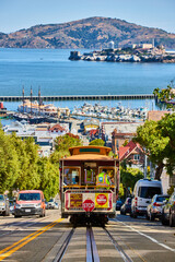 Trolley streetcar going down steep, sunny road with Alcatraz Island in San Francisco Bay, CA