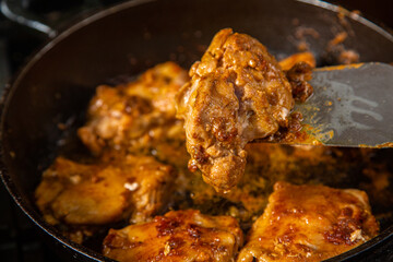 Chicken pieces in a sauce with spices in a frying pan with an iron spatula are turned over