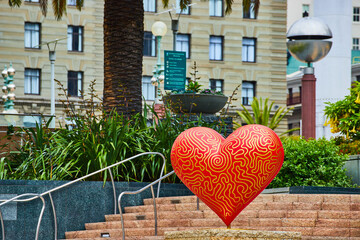 Red and yellow pride heart art on staircase with palm tree trunk in touristy Union Square in San Francisco, CA