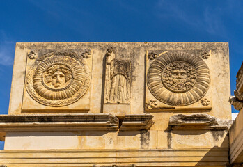 Frontal detail of the façade of the monumental portico with low reliefs and medallions with metopes of the old Municipal Forum of Augusta Emerita of Mérida, with two medallions and Medusa head. - obrazy, fototapety, plakaty