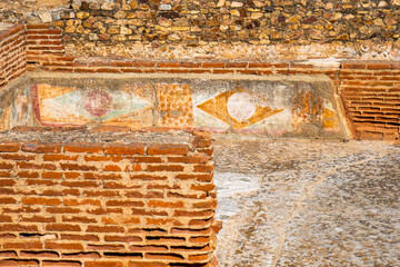 Detail of ancient geometric Roman paintings and frescoes and eroded earthy orange colors from the Mitreo Roman House of the Archaeological Complex of Mérida, Spain.