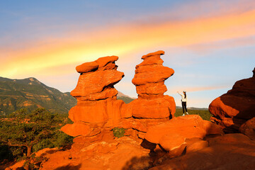 A hiker standing next to Siamese Twins at Sunrise at Garden of the Gods in Colorado Springs, Colorado. Garden of the Gods is a 1,341.3 acre public park located in Colorado Springs, Colorado, USA