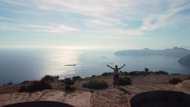 Young boy running over military ruins on top of a mountain. He runs up to the peak and raises his arms, looking at the sea and the mountains. Feeling of freedom and self-improvement. Monte Roldan 