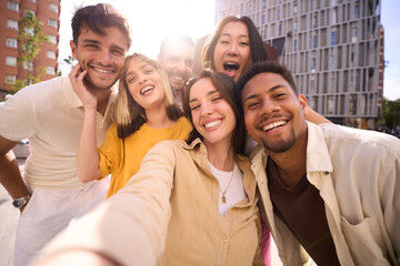 Selfie group of smiling multicultural young friends outdoors. Cheerful people posing happy for mobile photo hugging looking at camera all together. Positive relationships in community in generation z