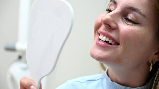 Happy woman looking at mirror enjoy healthy clean teeth beautiful smile after treatment at stomatology clinic. Pretty female patient and dentist doctor admiring result tooth whitening at dentistry 