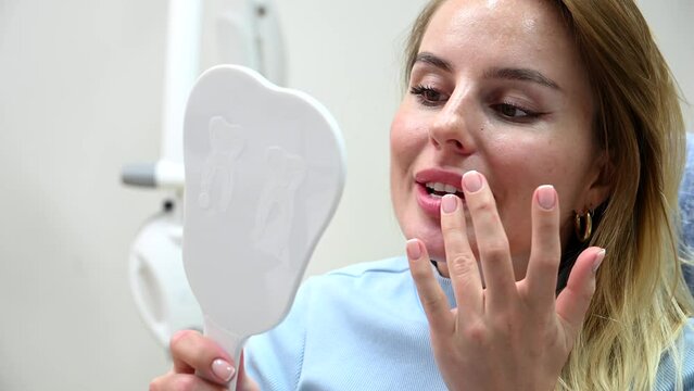 Young Beautiful woman smile after Dental Whitening process smile in mirror. Teeth whitening with UF Lamp, Led Lamp and gel in Dental Clinic. 4k 120 fps slow motion Raw footage