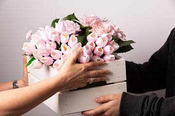 Manos regalando una caja con ramo de tulipanes rosas.