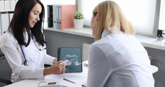 Doctor gynecologist showing woman patient ultrasound of fetus on digital tablet 4k movie slow motion. Pregnancy management concept