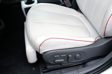 White leather driver seat with perforations and red stitching. interior of a modern car with white seats. White Electrically adjustable seat.