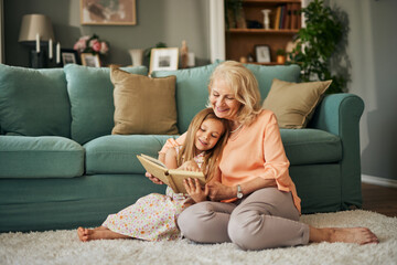 Grandma and granddaughter reading a book at home