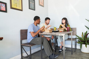 Friends eating takeout food at table talking and taking bites