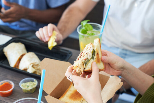 Friends eating takeout food at table holding sandwich
