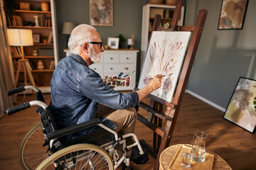 Senior man in a wheelchair painting at home