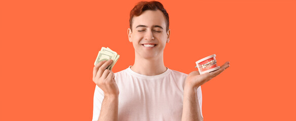 Young man holding jaw model with braces and money on orange background