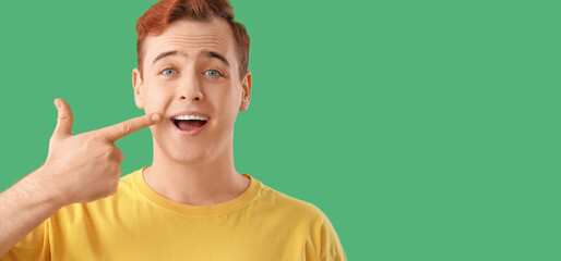 Smiling young man pointing at his teeth on green background with space for text