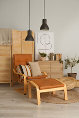 Cozy brown armchair with footstool and cushions in interior of living room