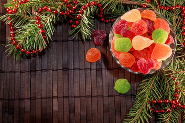 colorful jelly candies in a glass plate with christmas tree branches on a wooden dark background