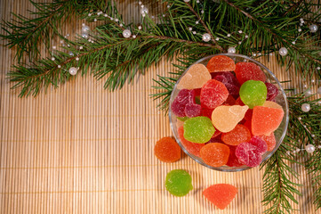colorful jelly candies in a glass plate with christmas tree branches on a wooden background top view