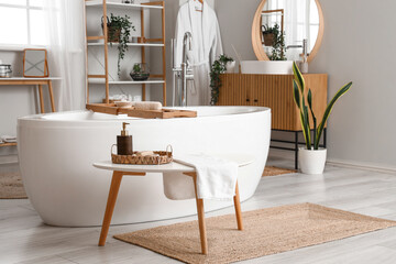 Fototapeta na wymiar Interior of light bathroom with bathtub and bathing supplies on table