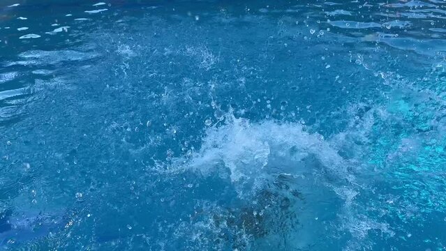 Slow motion video of happy boy of 9 years old jumping in the water of a swimming pool in the summer, blue water, smiling, and funny way.