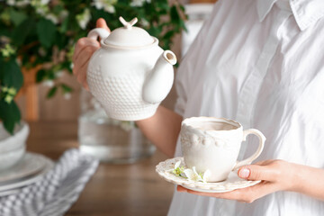 Woman preparing tea with jasmine flowers in kitchen, closeup