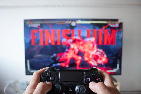  A male hand holding a play station 4 controller with mortal kombat fighter video game in a smart tv at background