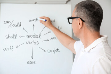 Male teacher writing English grammar on flip chart in classroom