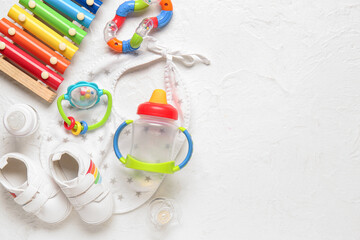 Stylish baby shoes with bib, toys, bottle of milk and pacifier on grunge white background
