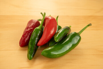 Capsicum annuum Jalapeno chilli hot peppers, group of green and red fruits on light brown wooden background