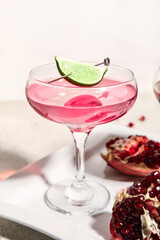 Glass of Cosmopolitan cocktail with lime and pomegranate on white background