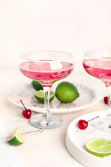 Glass of Cosmopolitan cocktail with cherries and lime on white background