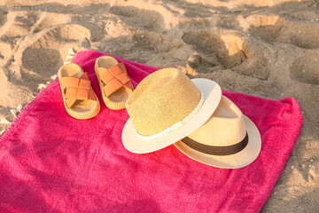 Towel with stylish straw hats and flip-flops on sand