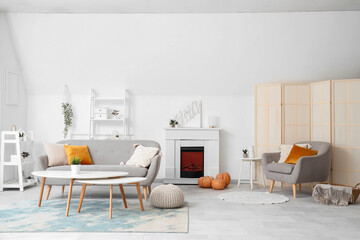 Interior of light living room with electric fireplace, pumpkins and sofa