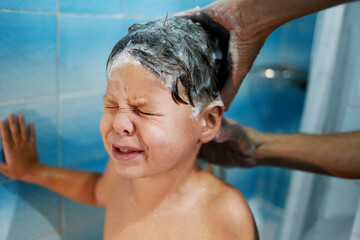 Dad's hands wash the little boy's head in the bathroom. The child does not like to wash his hair and cries.
