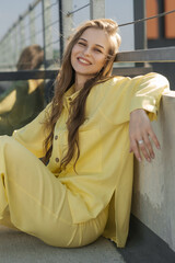 cute smiling female in a yellow summer outfit sitting outdoors