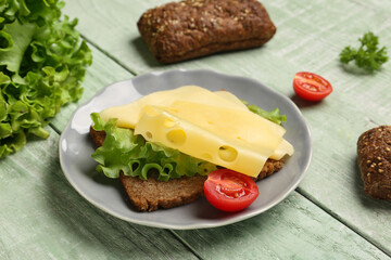 Tasty sandwich with cheese, lettuce and tomato in plate on green wooden background, closeup