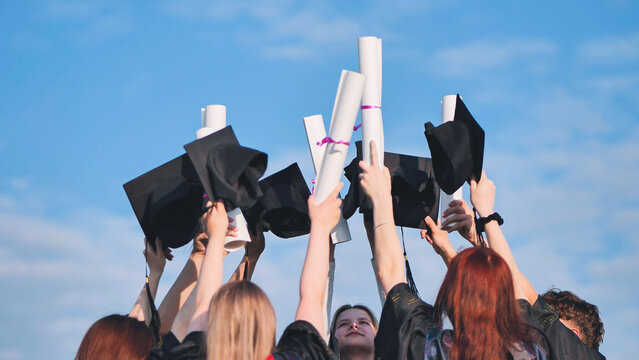 College graduates raise their hands with caps and diplomas to the sky.