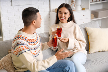 Happy couple with glasses of warm mulled wine sitting on sofa in living room