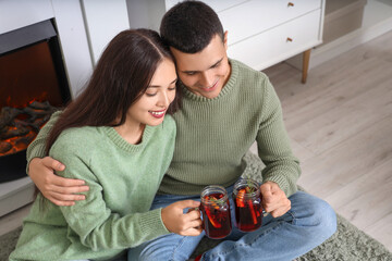 Happy couple with glasses of warm mulled wine sitting on floor in living room