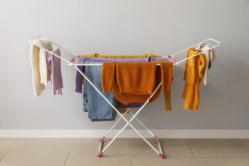 Clean winter clothes hanging on dryer near light wall