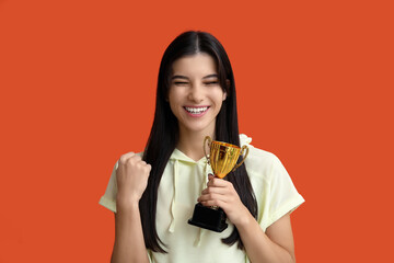 Sporty young woman with gold cup on orange background