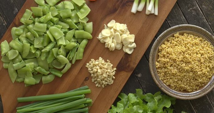 Ingredients for millet and vegetables stir fry: millet, garlic, ginger, scallions, carrot, sugar snap peas. Table spin.