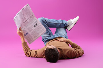 Young man with newspaper lying on purple background
