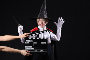 Little actor dressed as magician and hands with movie clapper on dark background